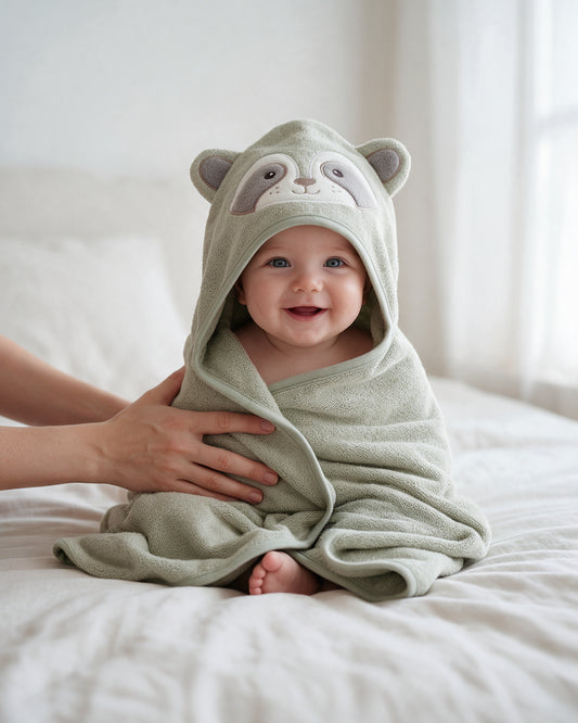Baby sitting on the bed in The Raccoon hooded towel
