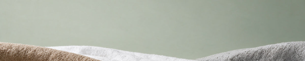 Toallas con capucha MiniBoo en arena, blanco y gris sobre una pared verde salvia suave