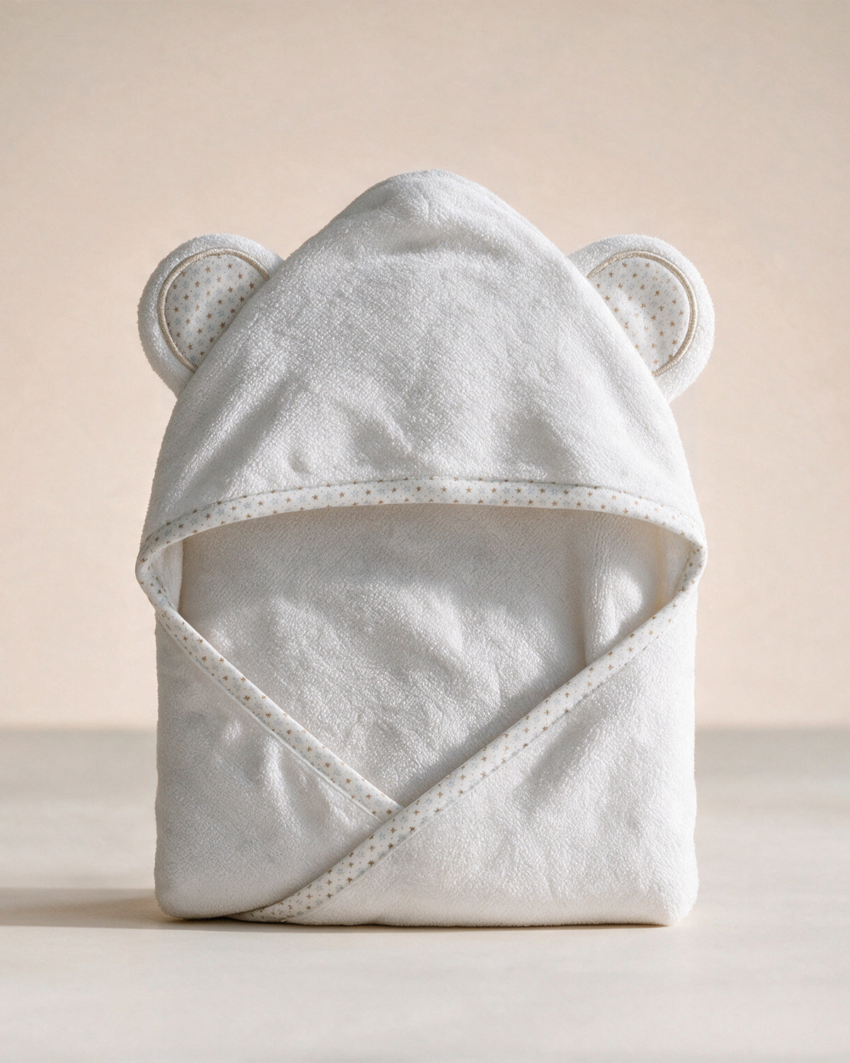 Starry Bear hooded baby towel in white with star-print ears and trim, on a cream background
