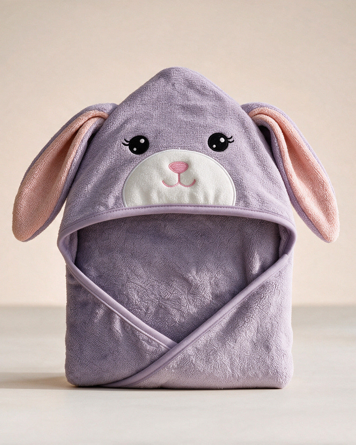 The Bunny hooded baby towel in soft lavender with long ears, on a cream background