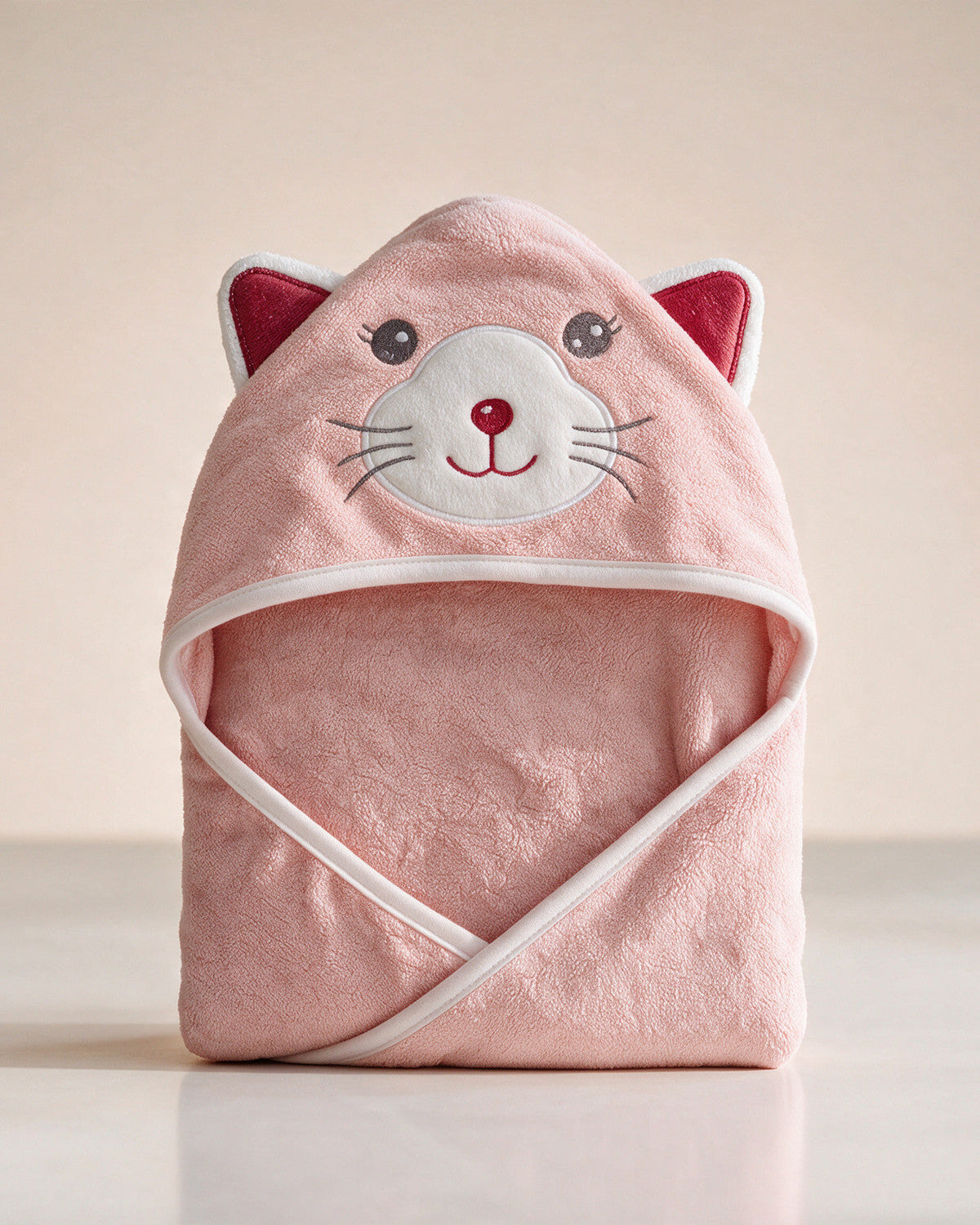 The Cat hooded baby towel in soft pink, standing on a cream background