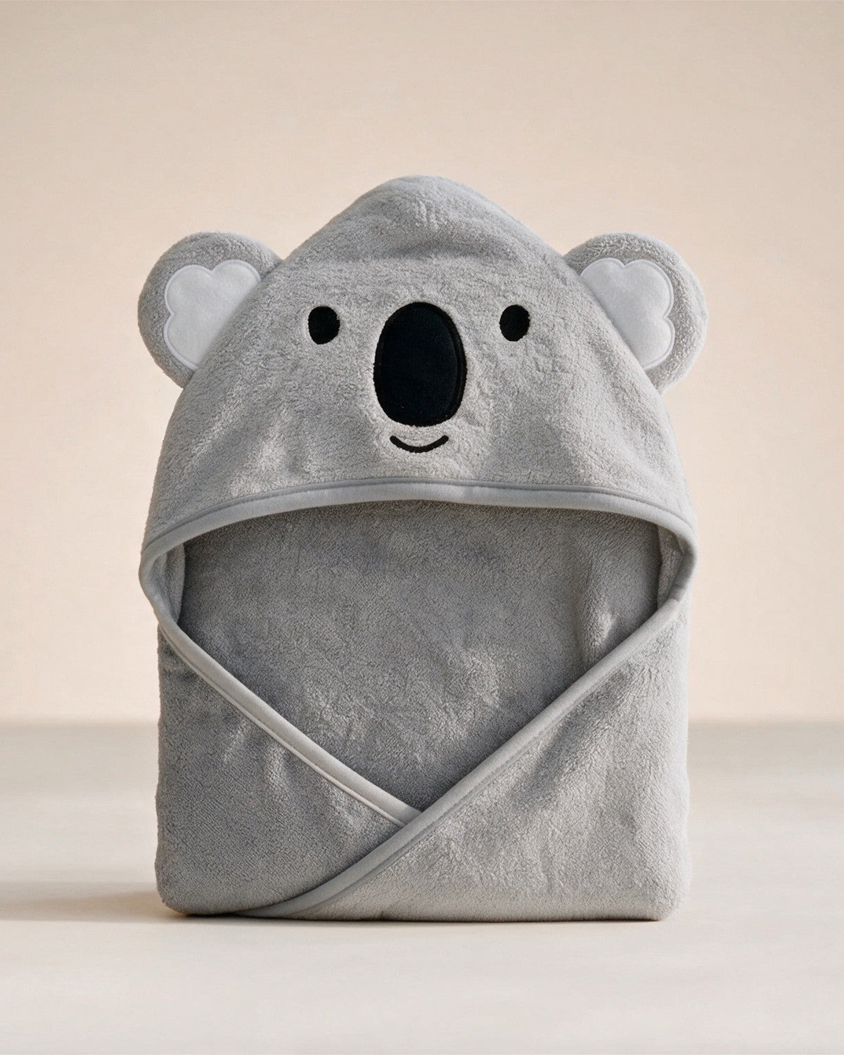 The Koala hooded baby towel in grey with open embroidered eyes, on a cream background