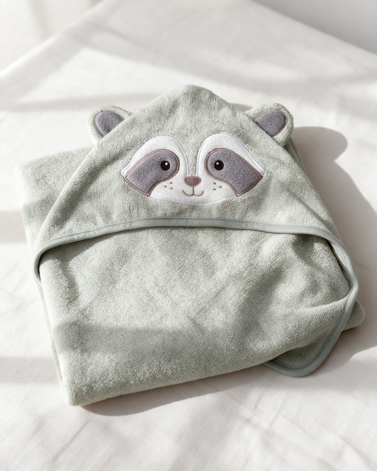 The Raccoon hooded towel folded on a white bed