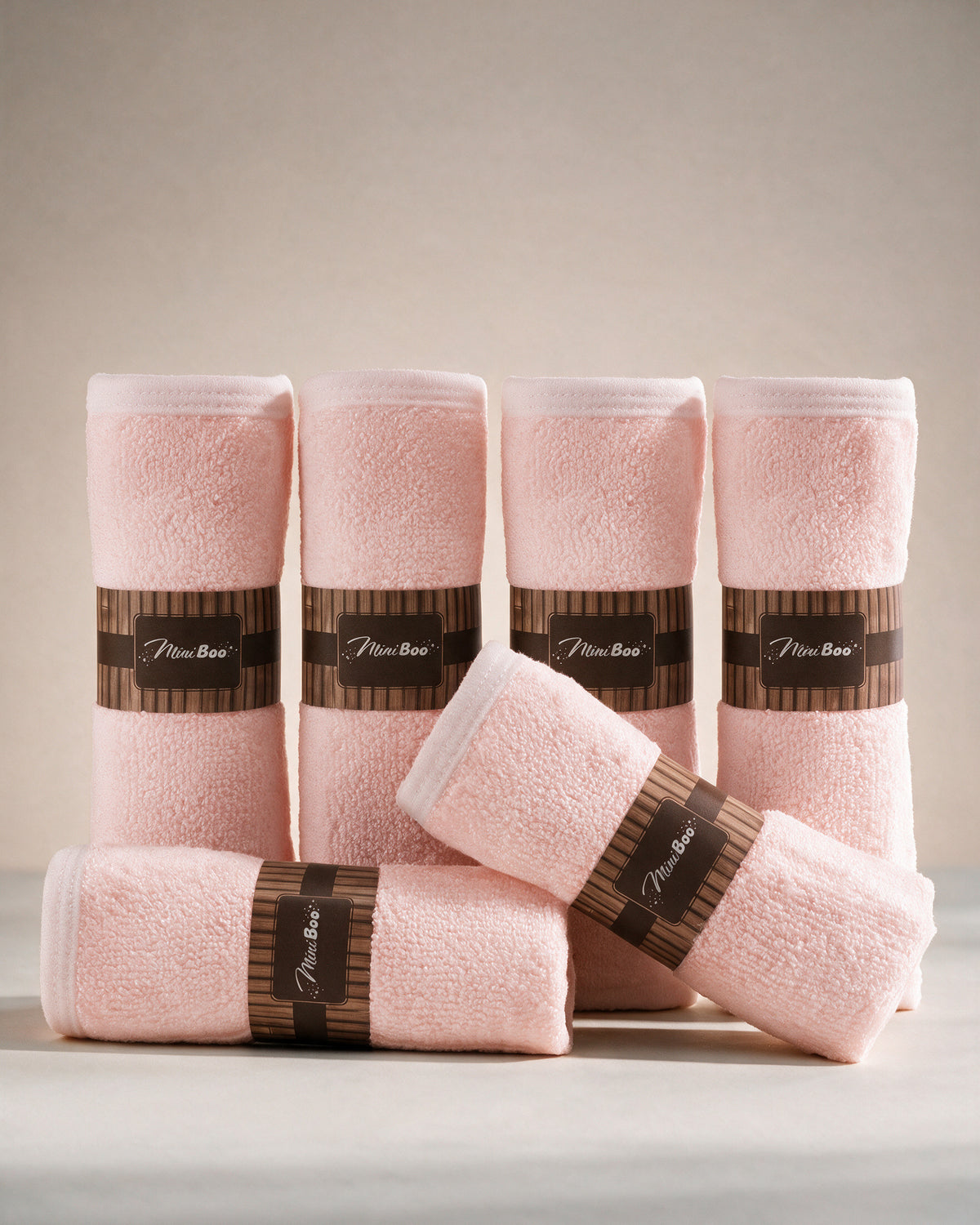 MiniBoo pink baby washcloths, a set of six rolled with brown paper bands, on a warm cream background