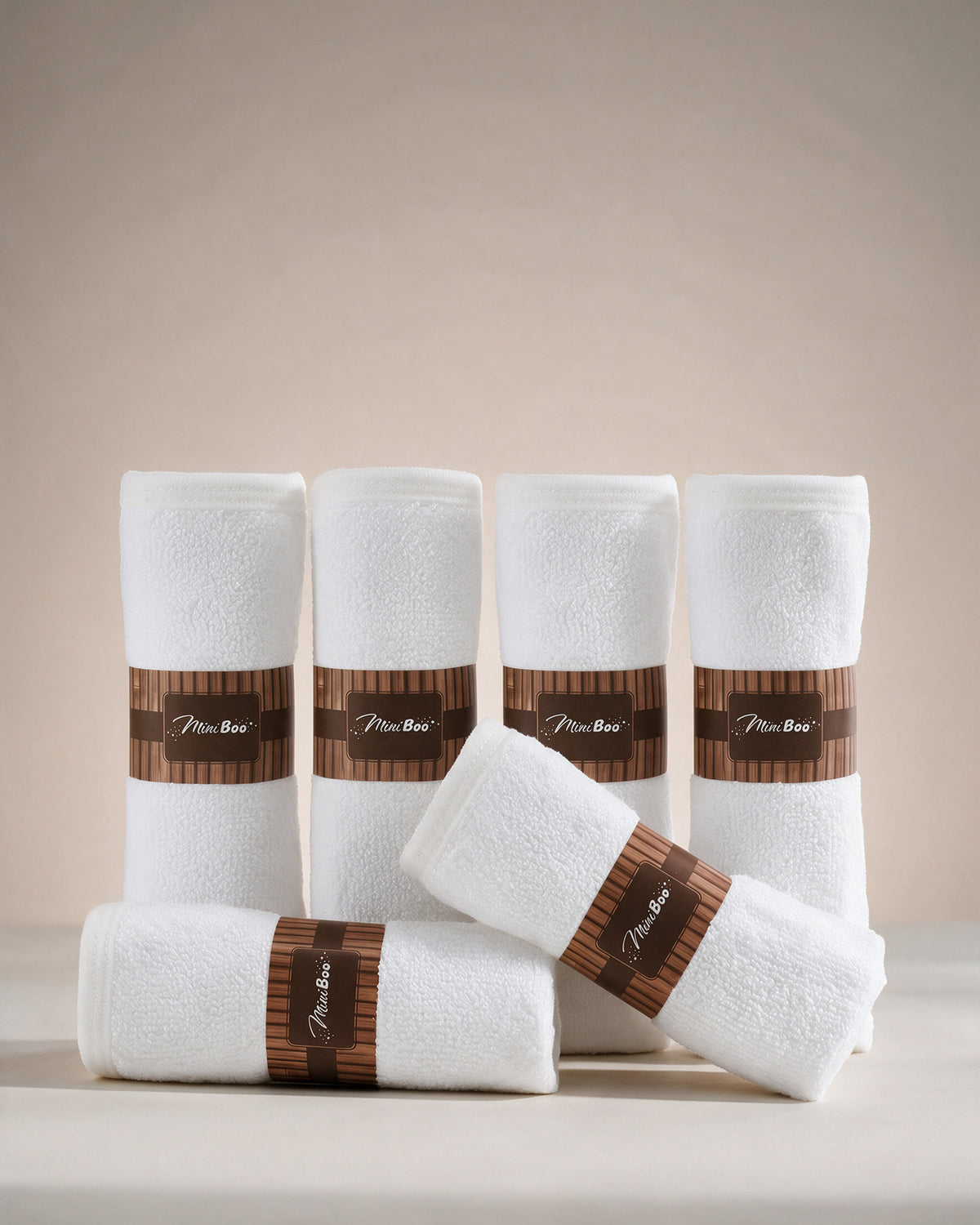 MiniBoo white baby washcloths, a set of six rolled with brown paper bands, on a warm cream background